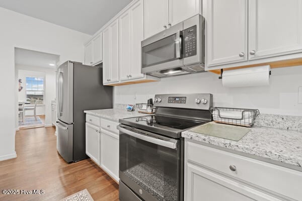 kitchen with white cabinetry, light stone counters, stainless steel appliances, and light wood-type flooring