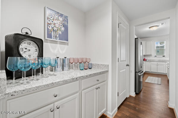 bar with stainless steel refrigerator, light stone countertops, dark wood-type flooring, and white cabinets