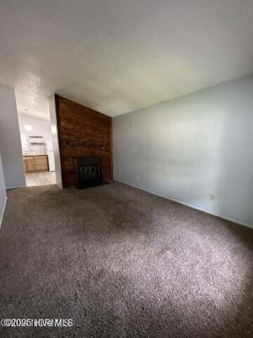 unfurnished living room featuring vaulted ceiling, a brick fireplace, and carpet floors