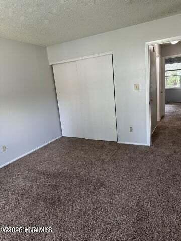 unfurnished bedroom with a closet, a textured ceiling, and dark colored carpet