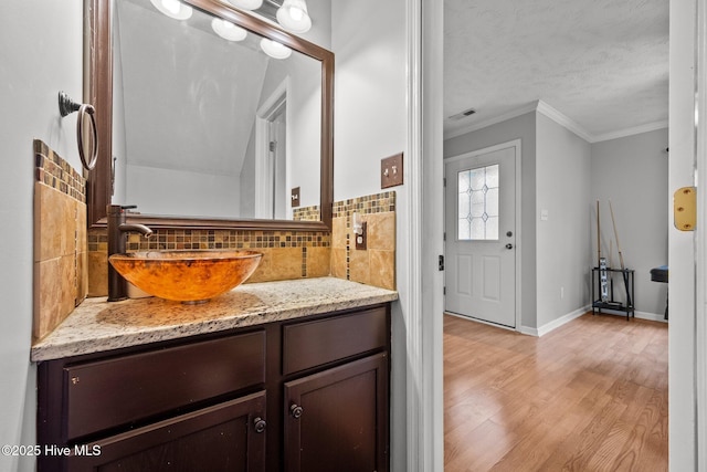 bathroom with crown molding, hardwood / wood-style floors, vanity, a textured ceiling, and decorative backsplash