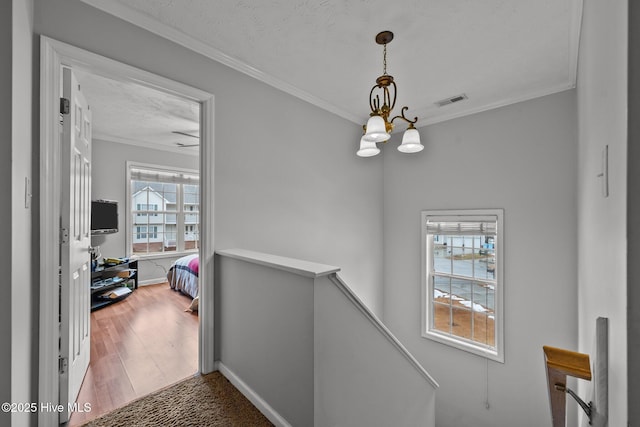 hallway featuring crown molding, wood-type flooring, a chandelier, and a textured ceiling