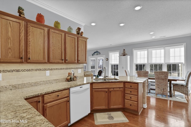 kitchen featuring dishwasher, sink, ornamental molding, light hardwood / wood-style floors, and kitchen peninsula