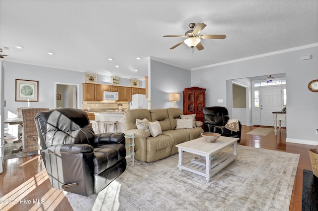 living room with a textured ceiling, ornamental molding, ceiling fan, and light wood-type flooring