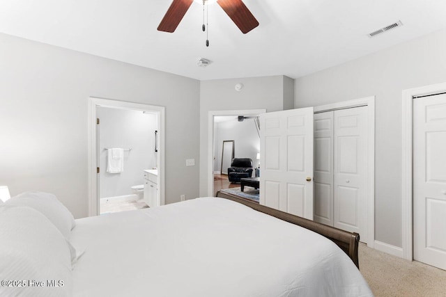 carpeted bedroom with two closets, ceiling fan, and ensuite bath