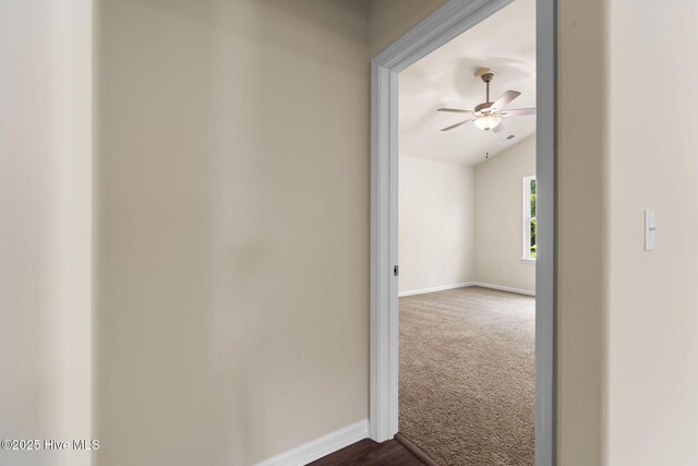 corridor with lofted ceiling, visible vents, dark carpet, and baseboards