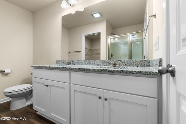 bathroom featuring a sink, toilet, a stall shower, double vanity, and wood finished floors