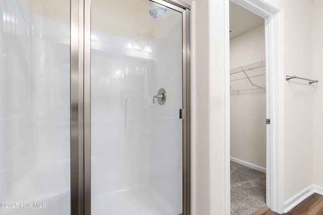 full bath featuring a stall shower, a walk in closet, and baseboards