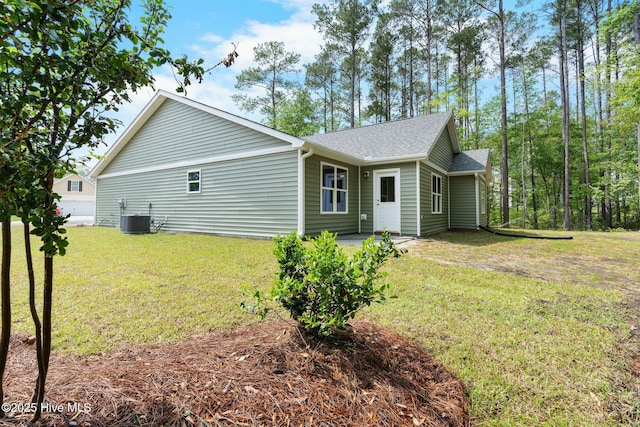 exterior space with a lawn, a shingled roof, and central air condition unit