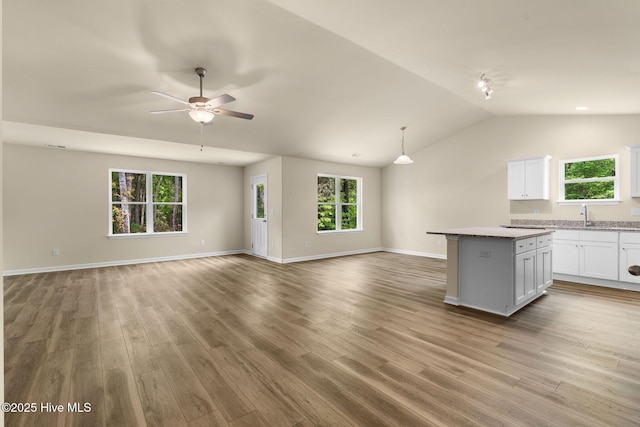 unfurnished living room with wood finished floors, a ceiling fan, lofted ceiling, and a sink