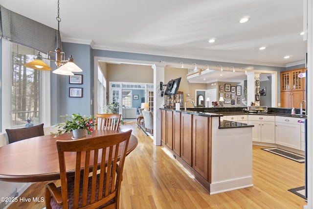 kitchen with decorative columns, ornamental molding, light hardwood / wood-style floors, white cabinets, and decorative light fixtures