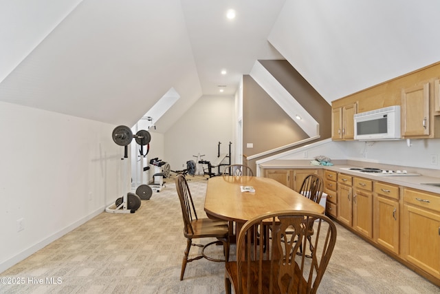 carpeted dining area with vaulted ceiling with skylight