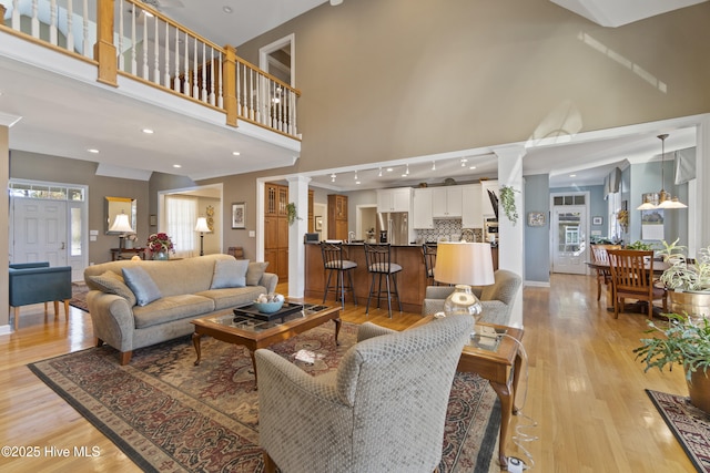 living room with light hardwood / wood-style flooring, ornamental molding, a high ceiling, and ornate columns