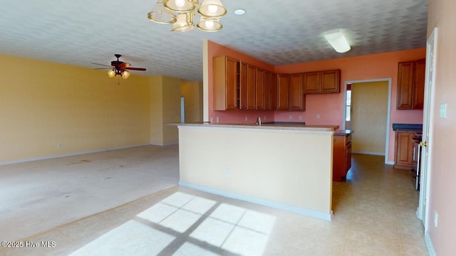 kitchen with sink, ceiling fan with notable chandelier, kitchen peninsula, and a textured ceiling