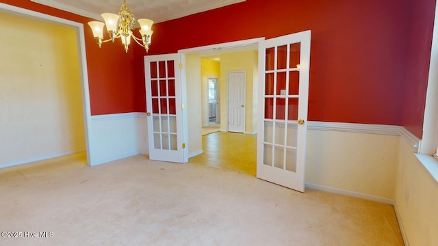 carpeted spare room with french doors, ornamental molding, and a chandelier