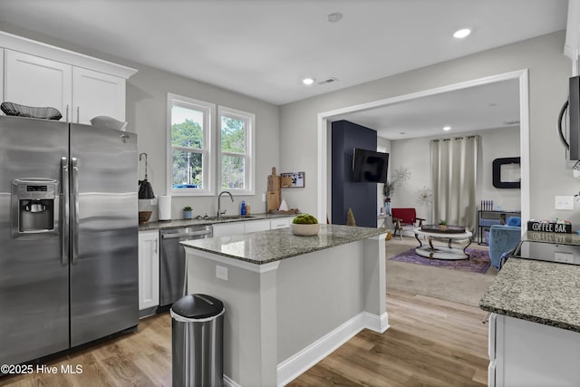 kitchen with appliances with stainless steel finishes, white cabinetry, dark stone counters, a center island, and light hardwood / wood-style flooring