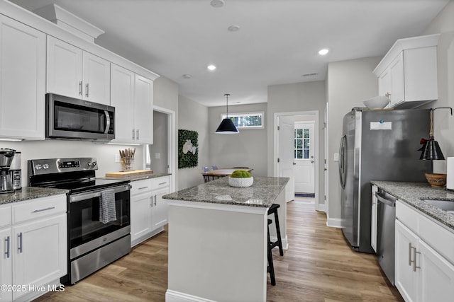 kitchen featuring a kitchen island, a breakfast bar area, white cabinets, stainless steel appliances, and light stone countertops