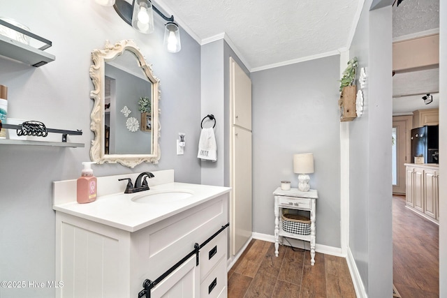 bathroom with baseboards, ornamental molding, wood finished floors, a textured ceiling, and vanity