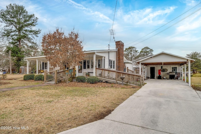 view of front of home featuring a chimney, a porch, a carport, driveway, and a front lawn