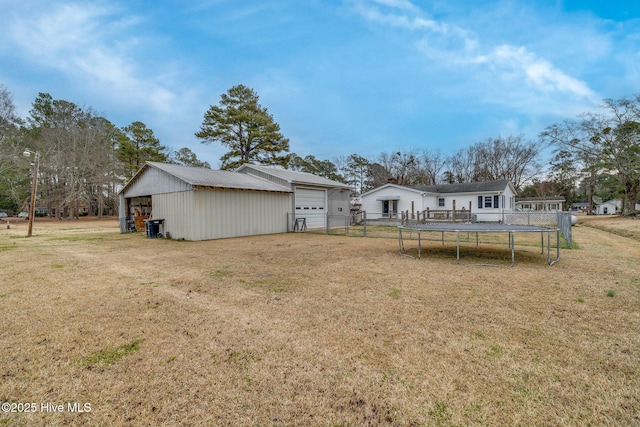 rear view of house with a yard, a trampoline, an outdoor structure, and a detached garage