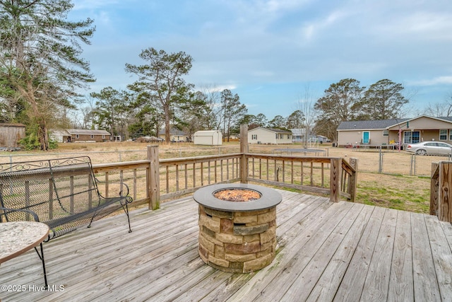 wooden terrace with a storage unit, an outdoor fire pit, fence, and an outbuilding