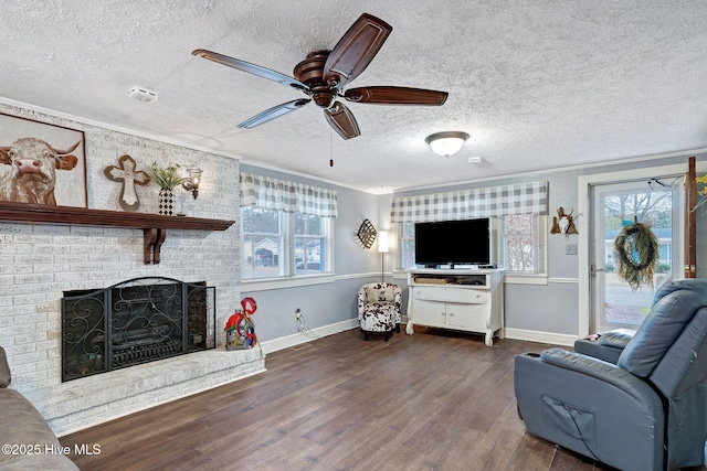 living room featuring a textured ceiling, wood finished floors, a ceiling fan, baseboards, and a brick fireplace