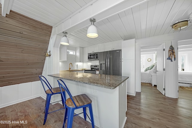 kitchen with stainless steel appliances, stone countertops, a sink, wood finished floors, and a peninsula