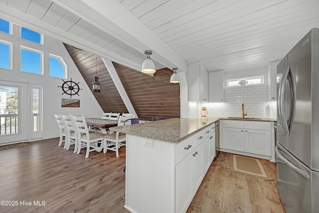 kitchen featuring a peninsula, white cabinets, light wood-style floors, freestanding refrigerator, and decorative backsplash