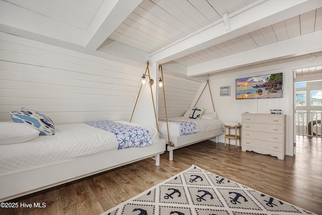 bedroom with beam ceiling, wooden ceiling, wooden walls, and wood finished floors