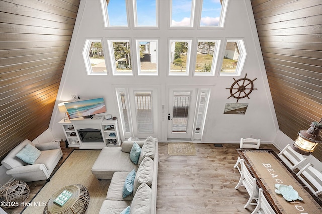 living room featuring a towering ceiling, wooden walls, and light hardwood / wood-style flooring