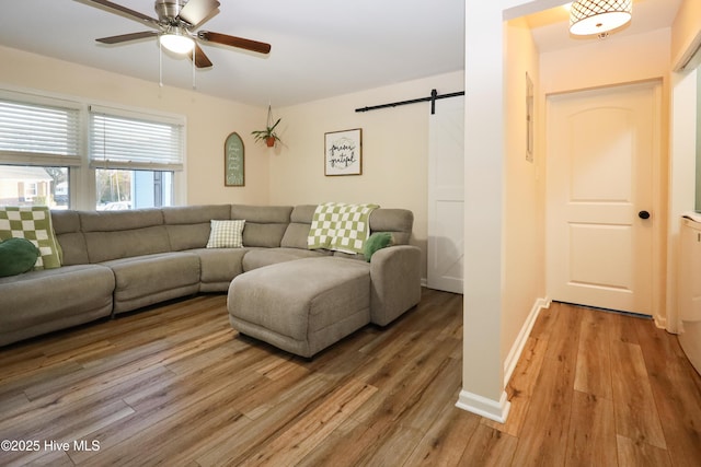 living area with light wood finished floors, a barn door, a ceiling fan, and baseboards