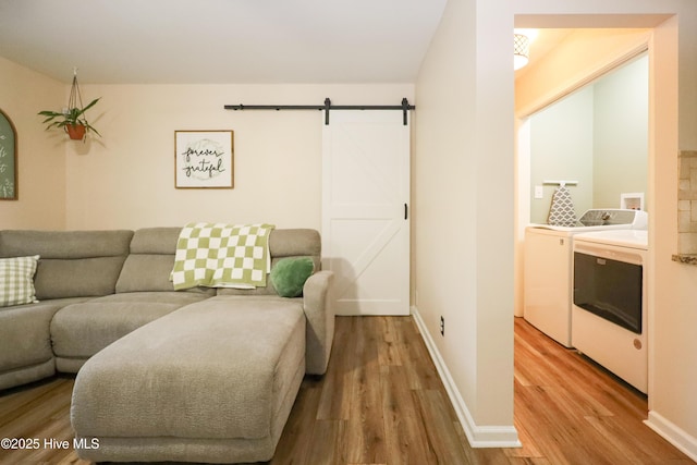 living room featuring a barn door, washer and clothes dryer, wood finished floors, and baseboards