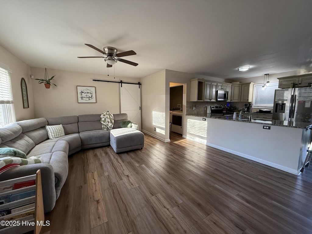 living room with a barn door, dark hardwood / wood-style floors, sink, and ceiling fan