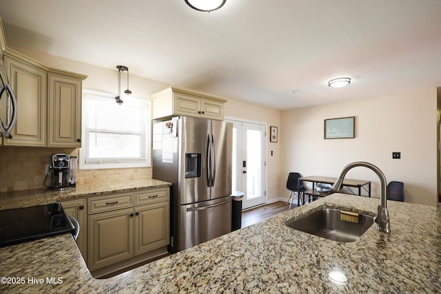 kitchen with light stone counters, pendant lighting, stainless steel refrigerator with ice dispenser, tasteful backsplash, and a sink