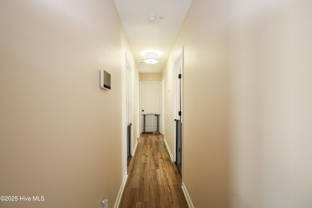 hallway featuring wood finished floors, attic access, and baseboards