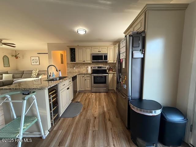 kitchen with sink, backsplash, light stone counters, kitchen peninsula, and stainless steel appliances