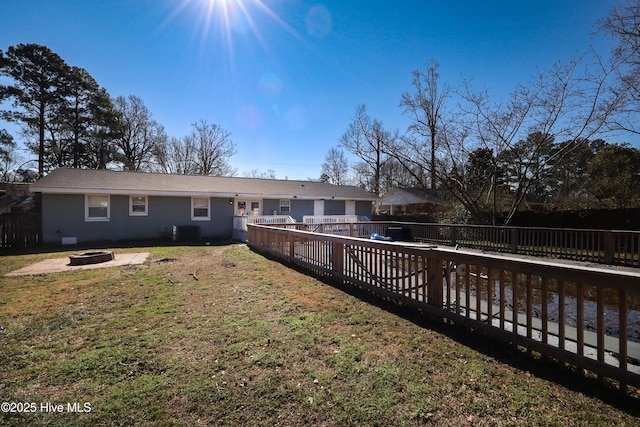 rear view of house featuring central air condition unit, a fenced backyard, a fire pit, and a lawn