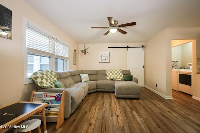 living area with a barn door, baseboards, dark wood-style floors, ceiling fan, and washing machine and clothes dryer