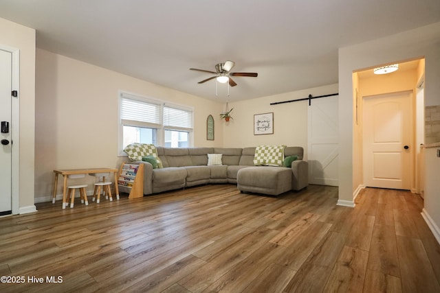 living room with baseboards, a barn door, a ceiling fan, and wood finished floors