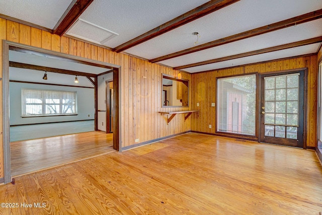 unfurnished living room with beam ceiling, a textured ceiling, and light wood-type flooring