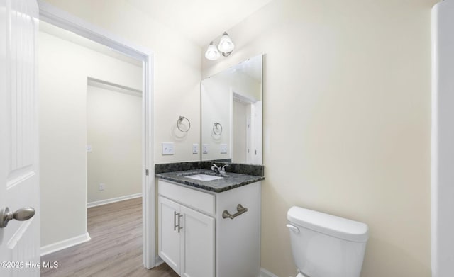 half bath featuring toilet, wood finished floors, vanity, and baseboards