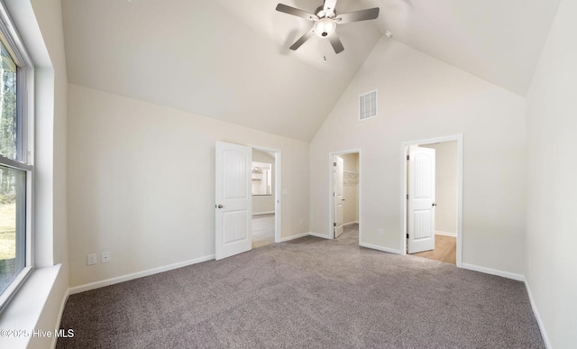 unfurnished bedroom with ceiling fan, a walk in closet, light colored carpet, and high vaulted ceiling