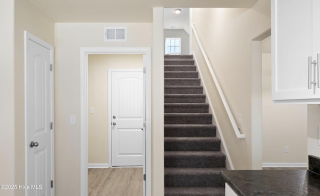 stairway featuring wood finished floors, baseboards, and visible vents