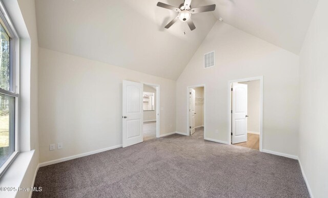 unfurnished bedroom with baseboards, a spacious closet, carpet flooring, visible vents, and high vaulted ceiling