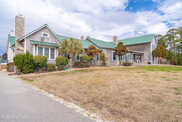 view of front of house featuring metal roof, a front lawn, a chimney, and a standing seam roof