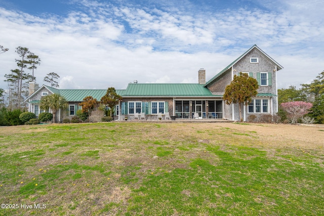 view of front of house featuring metal roof, a chimney, a yard, and a sunroom