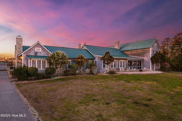 view of front facade featuring metal roof, a lawn, a chimney, and a standing seam roof