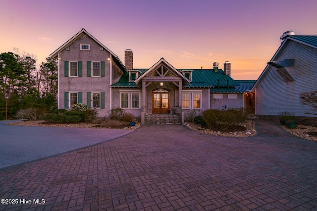 view of front of home featuring a standing seam roof, decorative driveway, french doors, metal roof, and a chimney