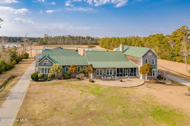 view of front of property with a standing seam roof, a sunroom, a chimney, a front lawn, and metal roof