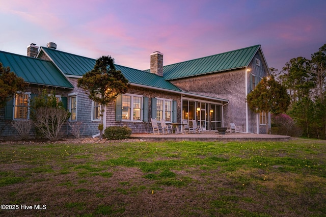 back of property at dusk with a yard, a patio, a chimney, and a standing seam roof